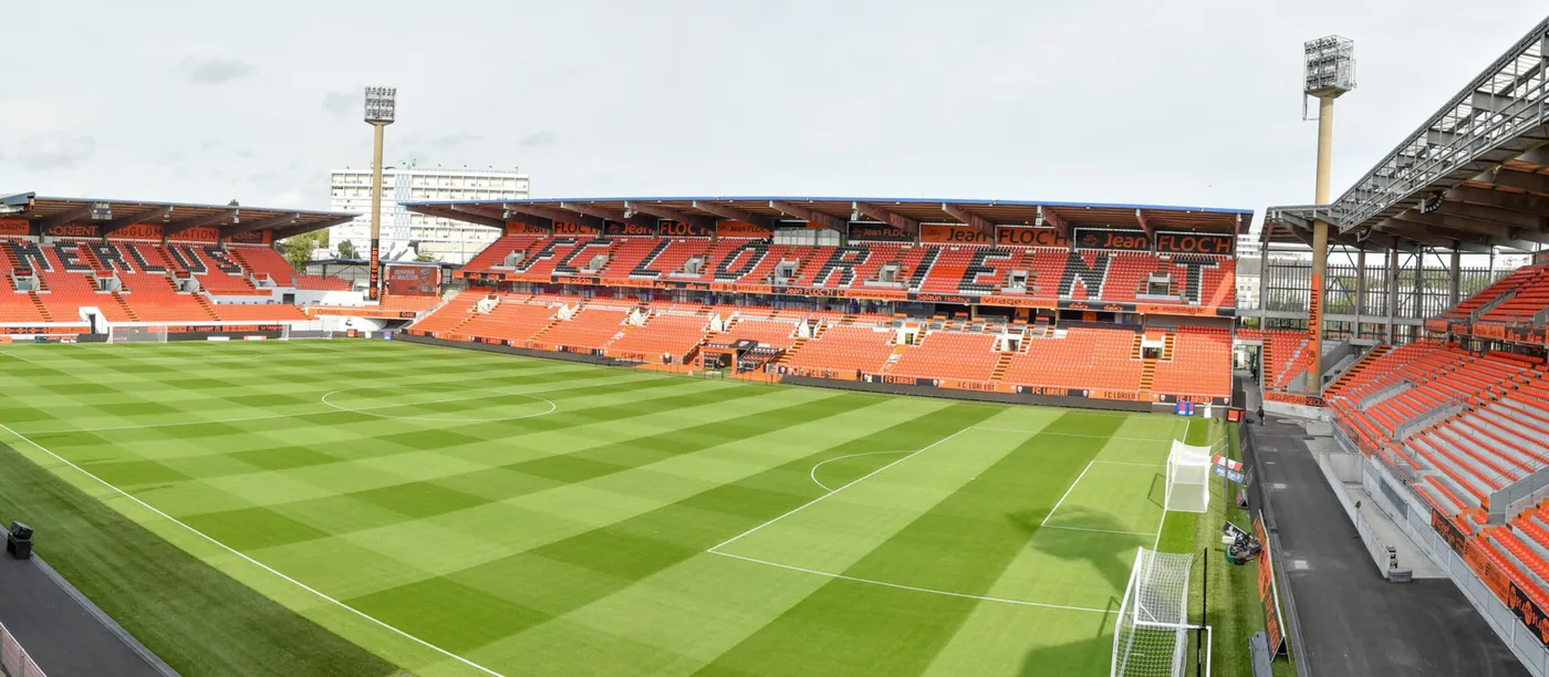 Panoramic view of the Stade du Moustoir in Lorient, with orange stands and LED boards around the pitch