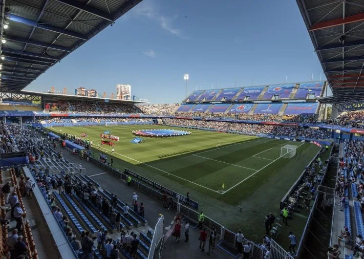Packed stadium stands on a match night, with LED boards around the pitch